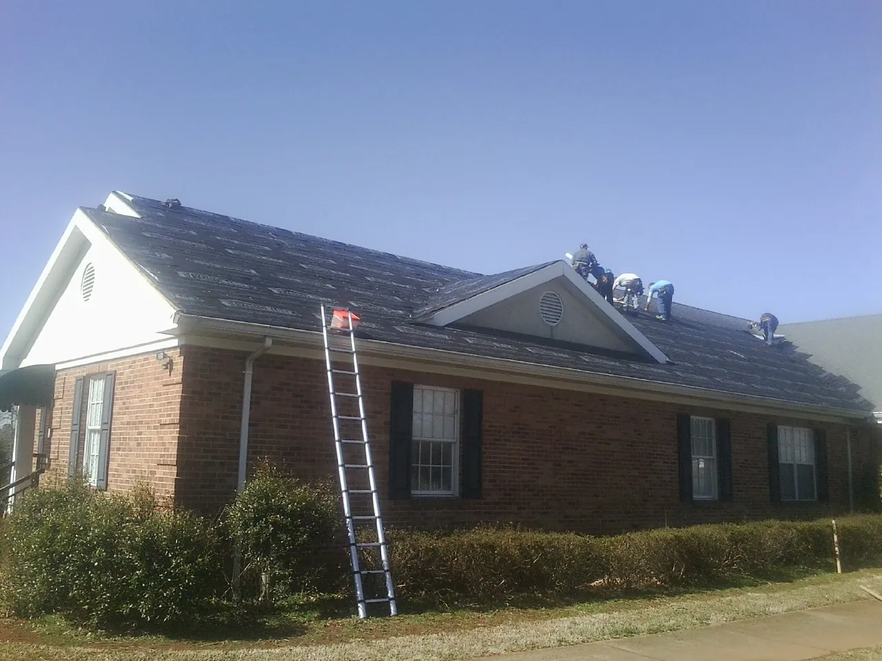 Crew tearing shingles off a brick ranch roof with a ladder set — Emergency Roof Repair work by our crew in Donaldson