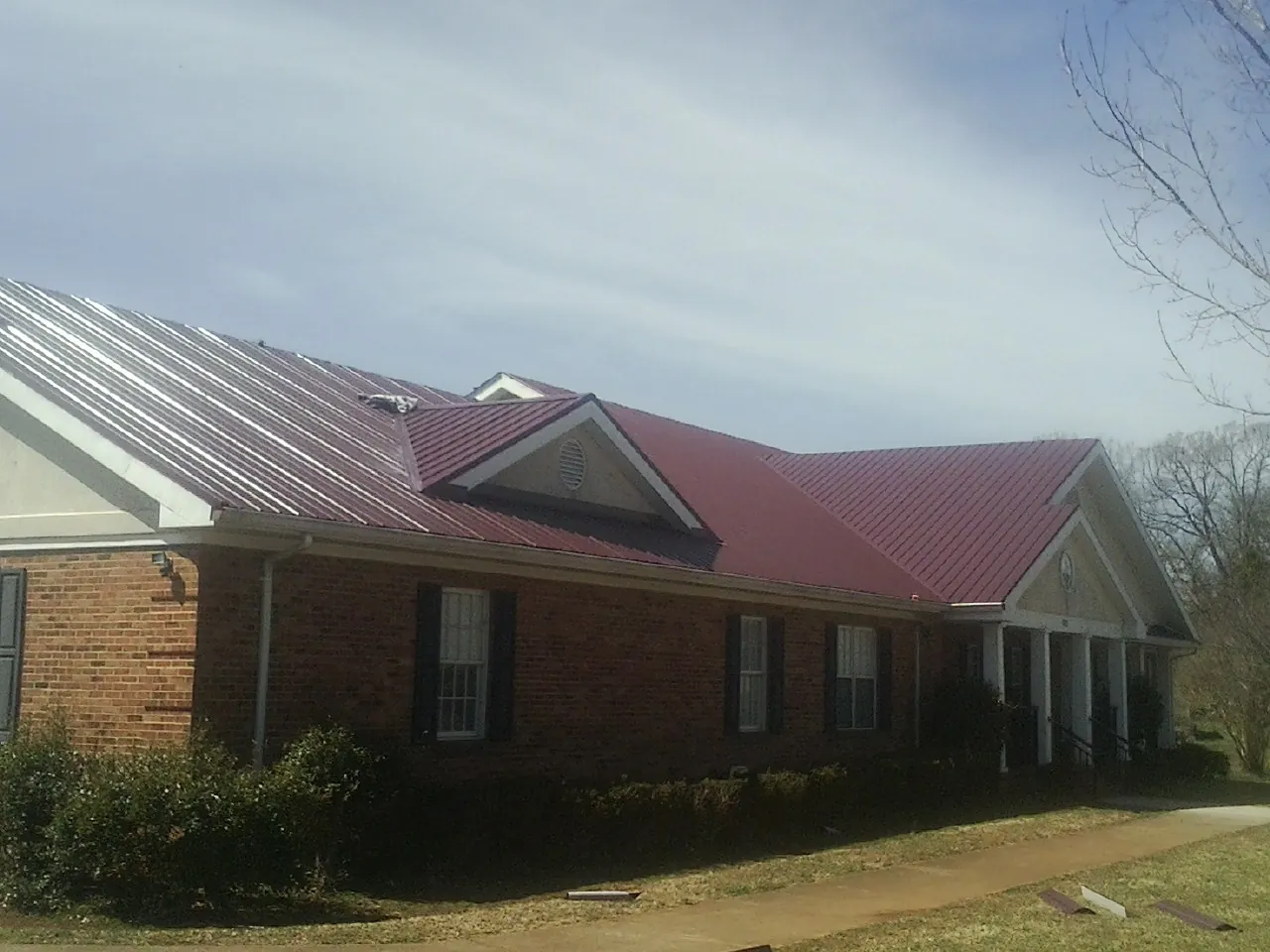 Red metal roof with gabled entries on a long brick building, from a Hail Damage Roof Repair job in Donaldson