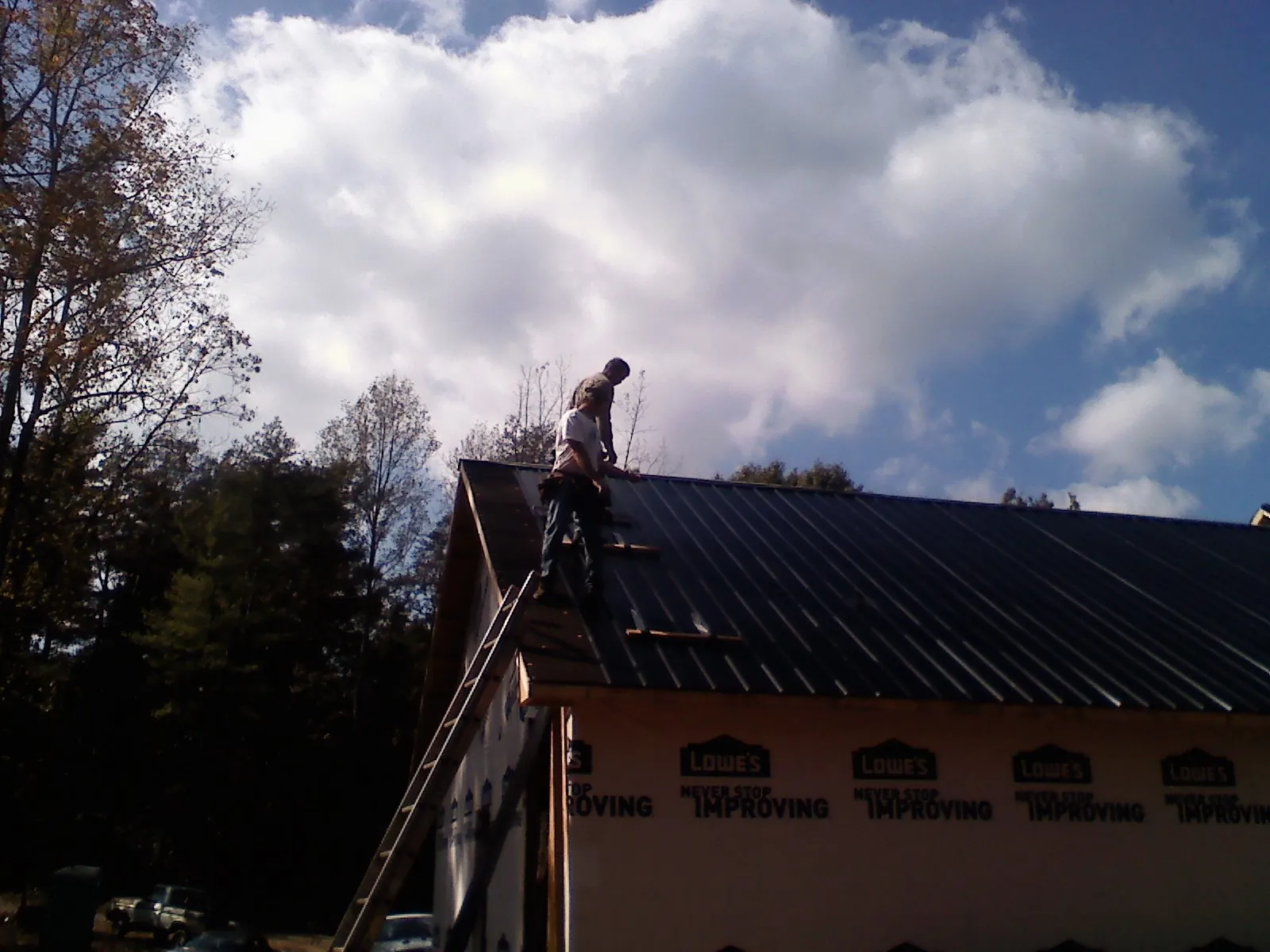Roofer fastening dark metal panels high against a cloudy sky, from a Roof Inspection job in Donaldson