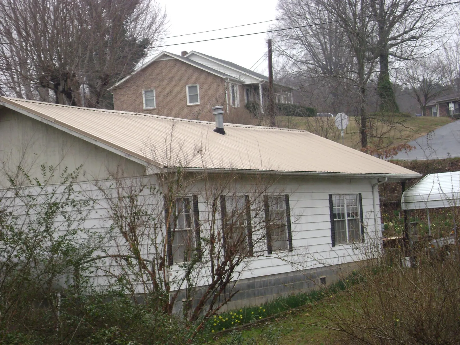 Tan metal roof on a white sided house set into a hillside — Commercial Roofing by Roofing Brothers in Donaldson