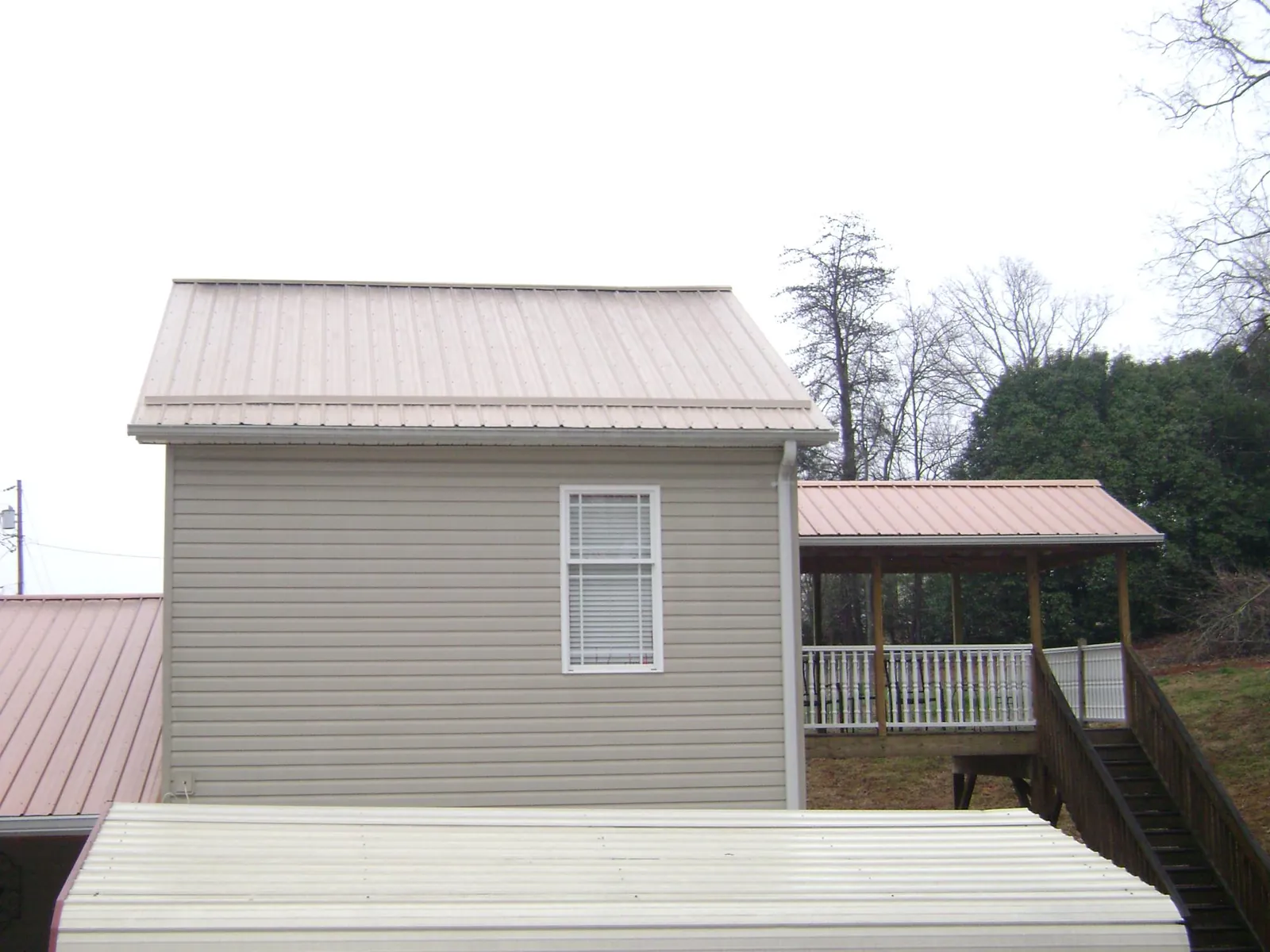 Tan metal roofs on a two story addition and attached porch, from a Roof Replacement job in Donaldson